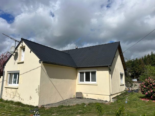 Maison de style simple avec un toit noir, jardin et ciel nuageux.