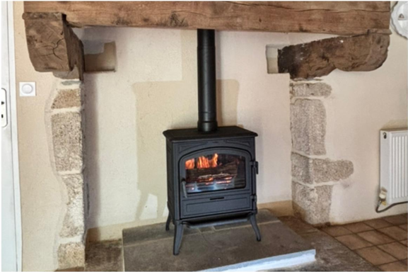 Poêle à bois noir sous un manteau en bois rustique dans une pièce claire.
